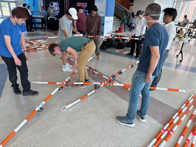 Students and a faculty member crouch on the atrium floor bolting striped barricade poles together into a star-shaped sub-assembly