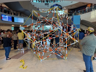 Crowd gathered around the completed sculpture in the atrium during the showcase, with more spectators lining the balcony above