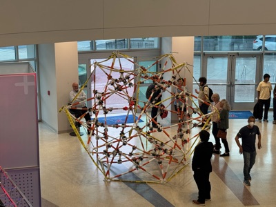 The completed sculpture seen from the second floor, with visitors walking around it near the atrium entrance