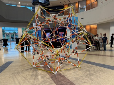 Front view of the completed sculpture showing the polyhedral pattern of poles and caution tape